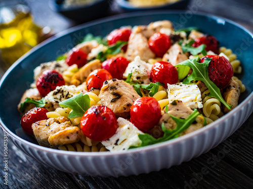 Roasted chicken nuggets, cherry tomatoes, feta cheese and fusilli served on wooden table 
