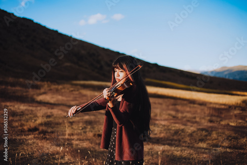 Mujer joven tocando violin en una montaña al atardecer. Concepto de personas y musica.