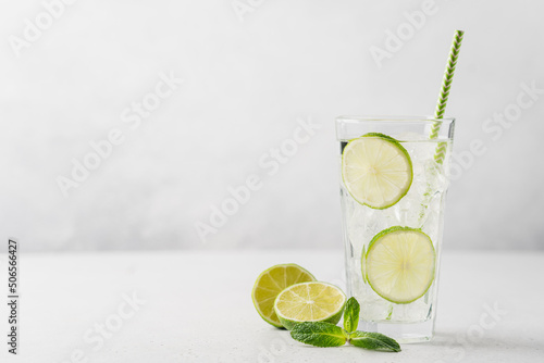 Lime mojito or lemonade with ice in tall glass with straw on light gray background with copy space. Summer refreshing drink