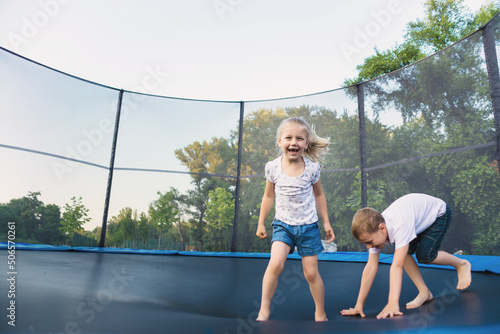 A boy and a girl jump on a trampoline without parental supervision. Brother and sister play on the trampoline in the park in summer