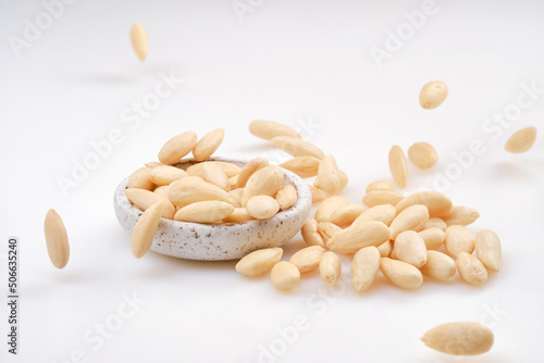 Pile of peeled or blanched almonds. Falling blanched Almonds. White bowl of peeled whole almonds on white background. Shallow depth of field
