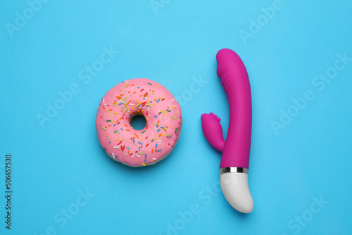 Pink vaginal vibrator and donut on light blue background, flat lay