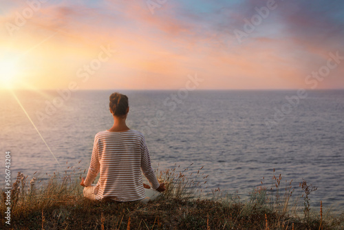 Woman meditating near sea at sunrise, back view. Practicing yoga