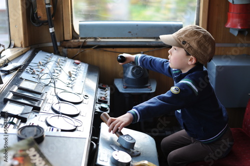 A young boy steering a locomotive and train in a driving compartment or cabin with handles and meters as a train driver, engine driver, engineman, locomotive driver, engineer, locomotive handler