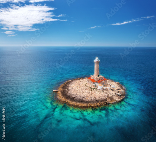 Lighthouse on smal island in the sea at sunny day in summer. Aerial top view of beautiful lighthouse on the rock, clear azure water and blue sky with clouds. Landscape. Adriatic sea, Croatia. Travel