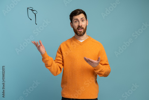 Young man wearing orange shirt throws glasses in trash isolated on blue background. Good vision concept. Stock photo