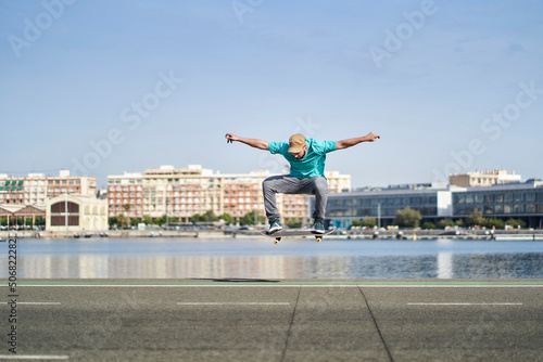 a man doing an ollie with his skateboard on an asphalt road next to the harbor