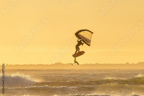 Focus on jump with wing foil equipment over a big ocean wave during sunset in Cape Town. Wing Foiling the new trend sport. Golden Background horizontal image with windy ocean and waves. 