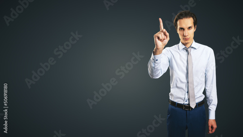 Young handsome man in shirt with raising up hand and forefinger isolated on abstract dark background with empty place for your logo or text, mock up