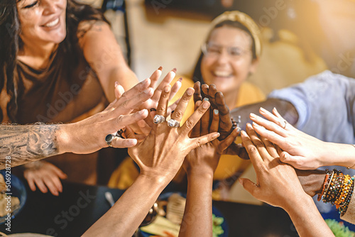 Adult friends in group, sitting around the dinner table high-fives all together celebrating friendship and to be united together - concept of lifestyle, trust, unity, togetherness - focus on hands