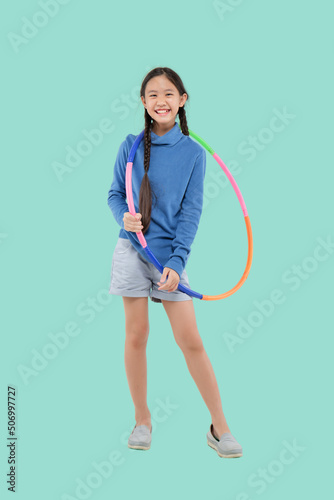 Portrait of happy little Asian child girl playing hula hoop on isolated pastel green background