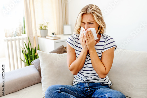 Shot of an attractive young woman suffering with the flu while sitting on her bed at home. The sick woman, holding a handkerchief, sneezing and feeling freezing, sitting on bed at home. Health problem