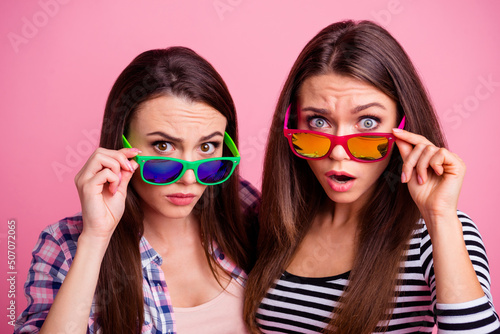 Portrait of two impressed confused girls touch glasses stare camera isolated on pink color background