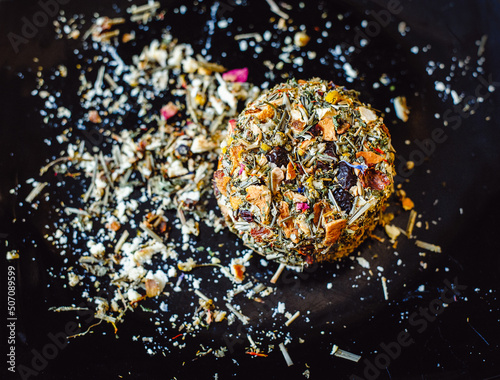 The round head of the French spicy cheese Boulette d'Avesnes sprinkled with different herbs, lies on a black plate. Close-up. Brin d'Amour