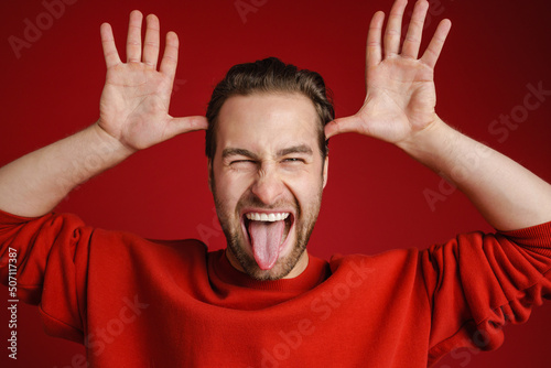 Young bristle man wearing sweater gesturing while showing his tongue