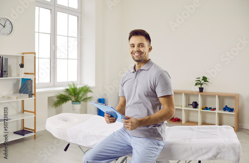 Portrait of smiling man masseur or physiotherapist in own medical office wait for client. Happy male therapist or osteopath in rehabilitation clinic on working day. Medicine and healthcare concept.