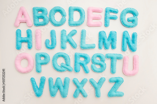 Full alphabet in capital letters made from stuffed felt on wooden floor background. Toy and implement for preschool and primary school kids learn to read. Montessori colors.