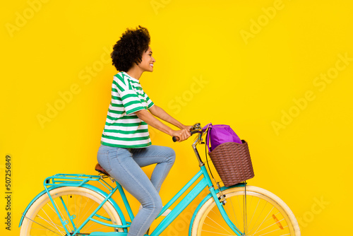 Profile photo of nice young lady ride bicycle wear t-shirt jeans bag isolated on yellow background