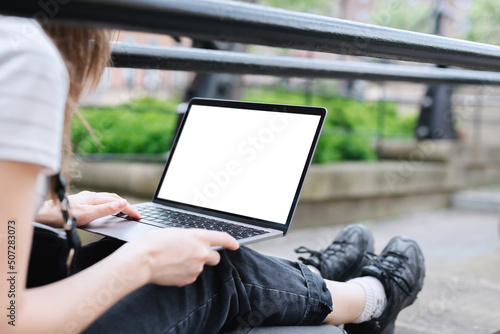 The girl works at a laptop, sitting on a stone parapet in the park. The girl works outdoors. Mockup of the laptop screen. A blank white netbook screen.