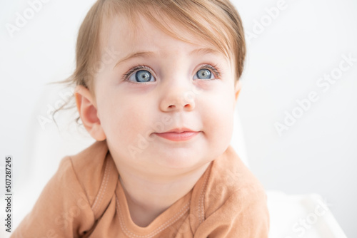 portrait of cute baby girl 10 months with blue eyes in brown bodysuit on white background