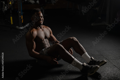 Afro american man doing abdominal exercises in a dark studio. 