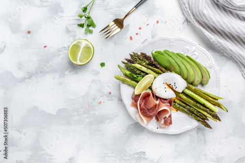 Delicious breakfast or snack of asparagus, avocado, poached egg and prosciutto, jamon, bacon on light background. Keto paleo lunch, Top view