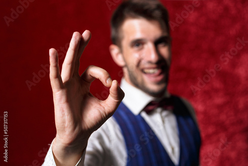 Positive man in suit and bow tie showing ok sign on red background in studio 