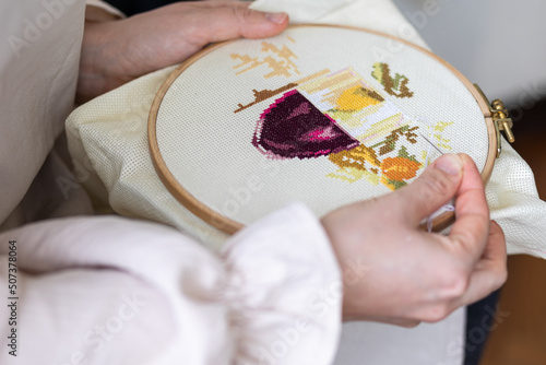 Cross-stitch embroidering in progress. Young girl in linen clothes is doing handmade embroidery