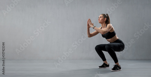 Sports woman in fashion black sport clothes squatting doing sit-ups in gym, over gray background