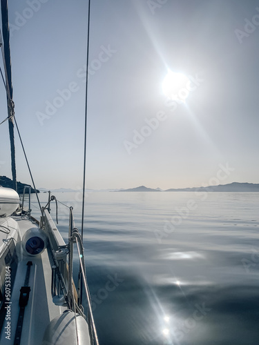 View from the yacht on Beautiful view of the calm sea in the morning. Sailboat in Aegean sea. Yacht sailing in an open sea. Close-up view from the deck to the bow and sails.