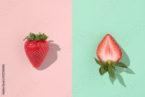 One whole and one sliced strawberry on a pastel pink and tiffany green background with sharp shadows. Minimum summer concept