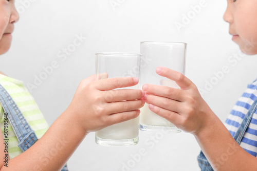Two little sisters drinking tasty milk from glasses isolated on white background. Happy 6- and 5-year-old sisters drink healthy milk before school.