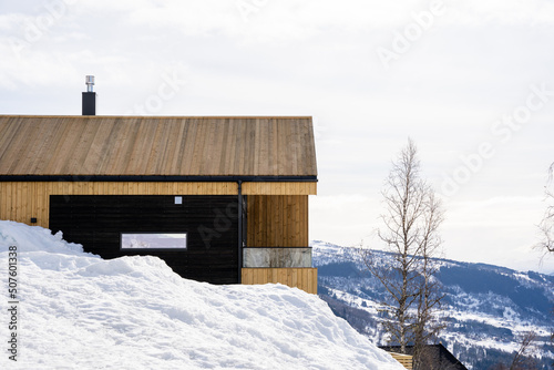 Wooden holiday home in the mountains of Norway in winter, where there is a lot of white snow and fluffy white clouds in the beautiful blue sky