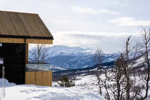 Wooden holiday home in the mountains of Norway in winter, where there is a lot of white snow and fluffy white clouds in the beautiful blue sky