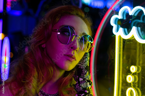 Long hair girl with sunglasses and leather jacket looking at neon lights 