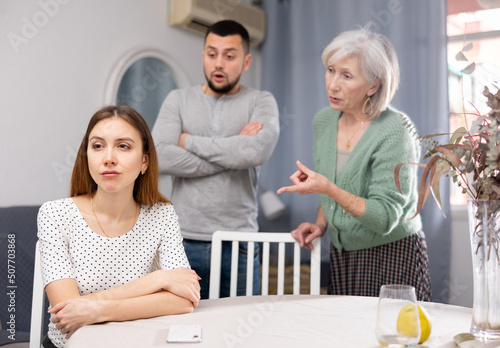 Woman ignoring her husband and mother-in-law standing behind and arguing with her at home.