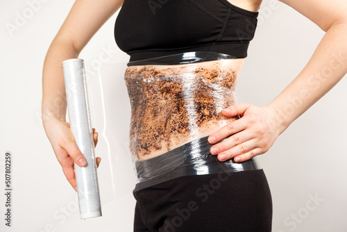 A woman makes a belly wrap with a coffee anti-cellulite body scrub. The concept of weight loss and skin care