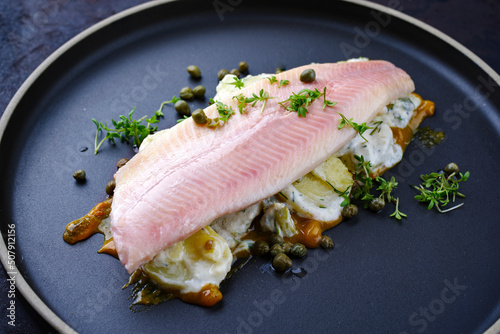 Modern style traditional smoked rainbow trout with boiled potato salad, yoghurt and mustard served as close-up on a Nordic design plate