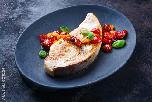Fried swordfish steak with tomatoes and paprika served as close-up on a design plate