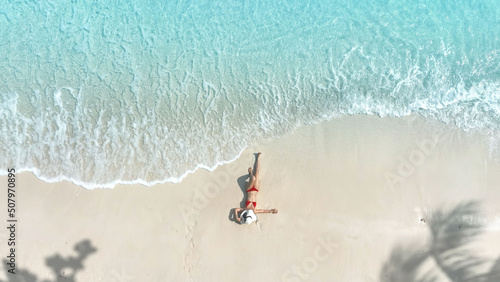Aerial view of woman body in bikini sunbathing as laying on the beach, blue sea water in background -Summer fashion concept