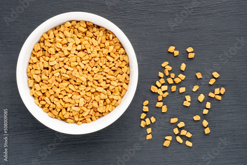 Fenugreek (Trigonella foenum-graecum) in ceramic bowl and bunch on black wooden background. Macro. Flat lay. Vegetarian food concept