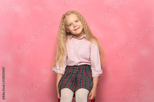 little girl schoolgirl sits in a chair. Pink background.