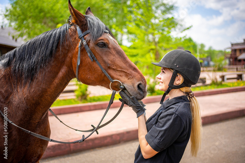 Lovely young woman wearing helmet stroking to her brown horse