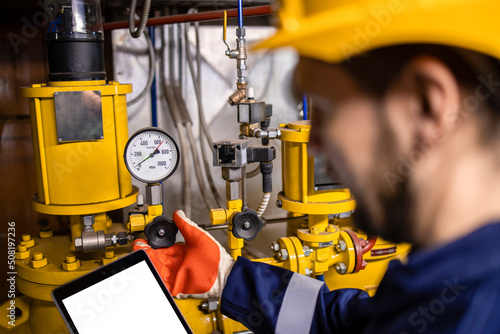 Oil and gas refinery worker measuring pressure of gas pipes and checking tablet computer.