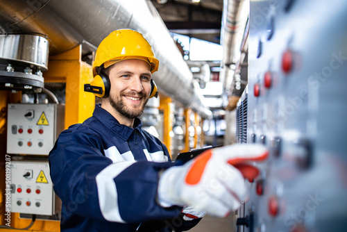 Smart caucasian factory worker wearing hardhat, earmuffs and working in power plant.