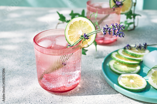 Cool lavender lemonade with lime slices and lavender flower on the table near pastel light blue background. Healthy organic summer soda drink. Detox water. Diet unalcolic coctail.