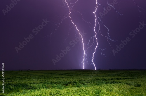 Bright lightnings in dark stormy sky above green field, climate change or weather forecast concept image