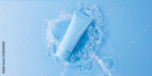 Blank tube of skincare product and splashing water on blue background upper view
