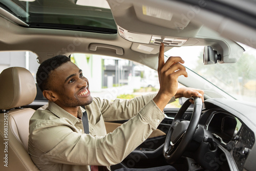 Man sitting in car pushing buttons, opening car sunroof or inspecting car. 