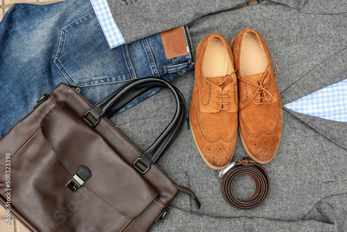 A pair of brown suede derby shoes, blue jeans, leather and bag belt with grey tweed blazer. Casual business outlook. Top view. 
